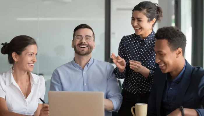 Cuatro personas en una oficina mirando la pantalla de un portátil y riéndose