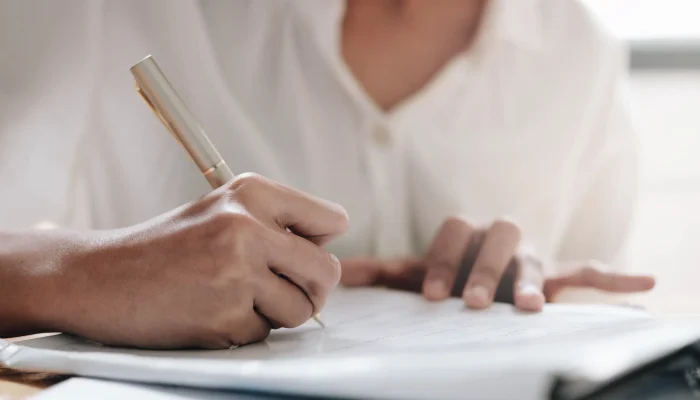 Primer plano de una mano escribiendo sobre una hoja con un bolígrafo elegante